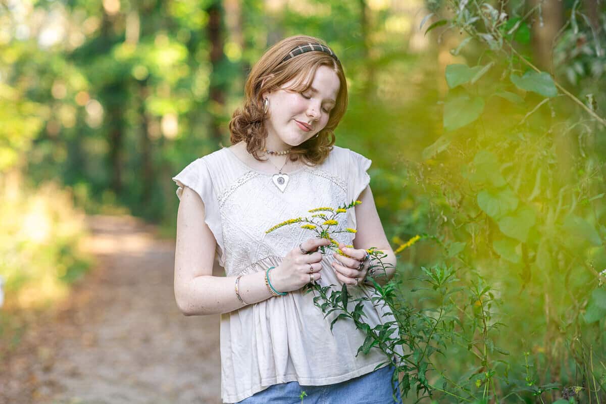 teenage girl holds yellow flower in the woods