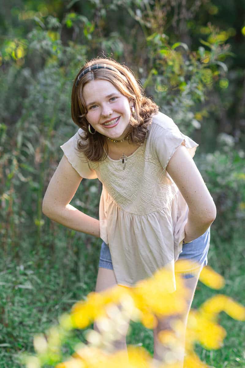 teenage girl poses in woods with yellow flowers and laughs