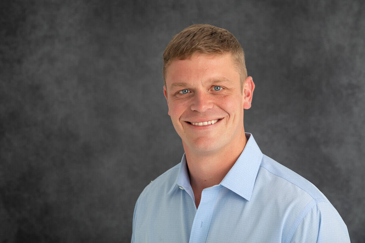 Man in blue dress shirt poses for headshot against gray background