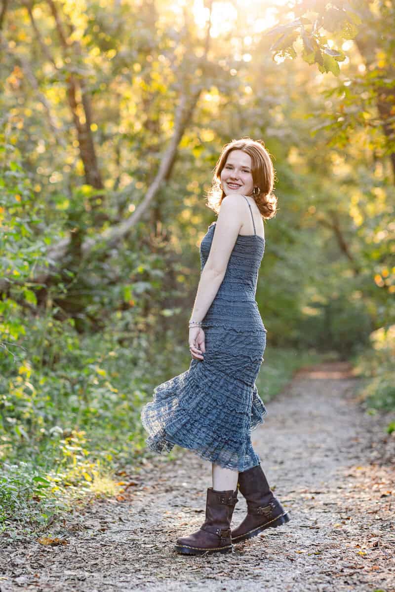teenage girl in blue dressdances in woods with sunlight behind her