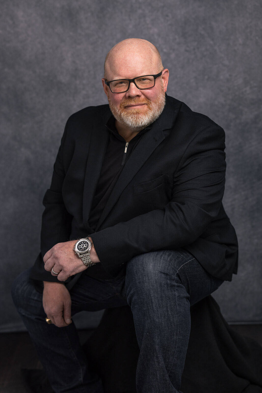 Man in black jacket poses for headshot seated