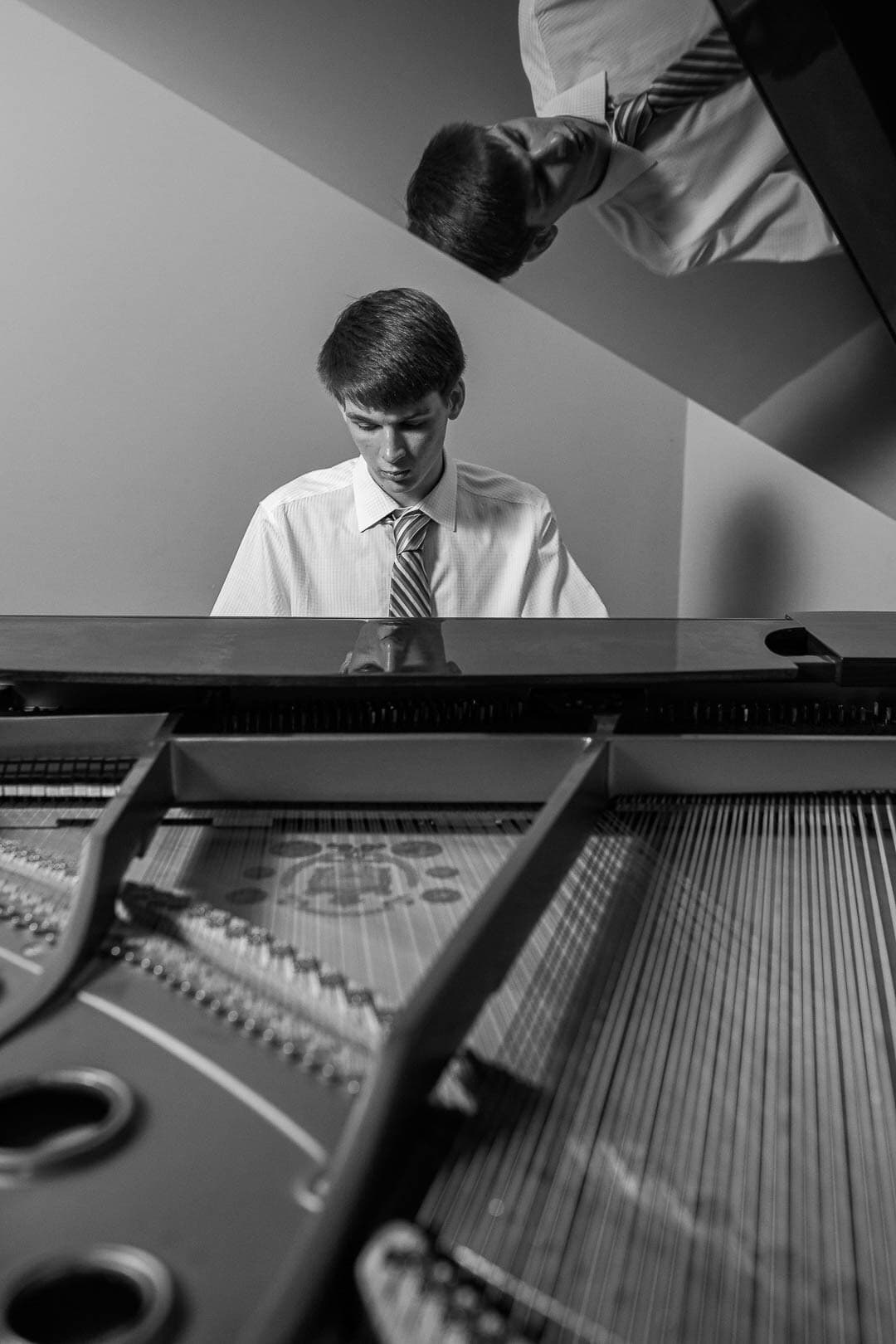 View of young man playing piano with reflection on shiny grand piano