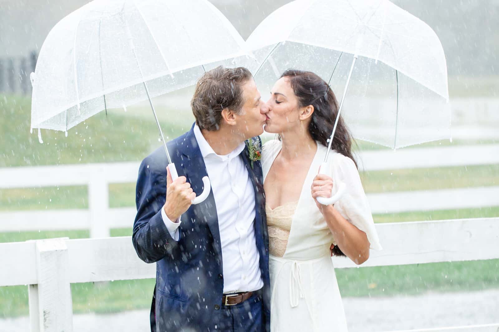Elopement bride and groom stand under umbrellas kissing outside in pouring rain.
