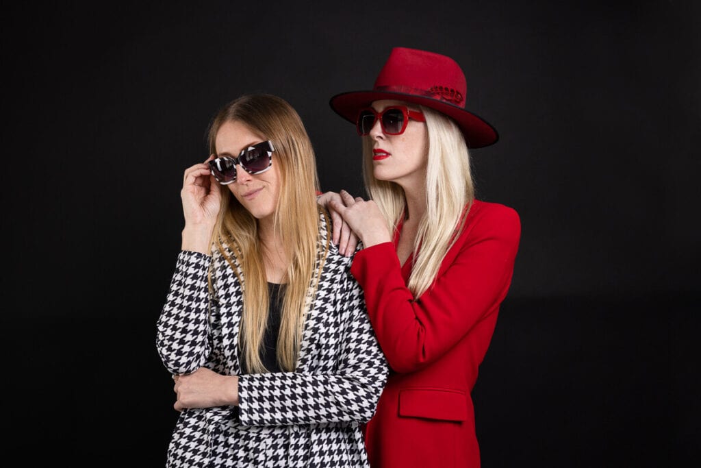 two women in sunglasses against black background pose for fashion photos