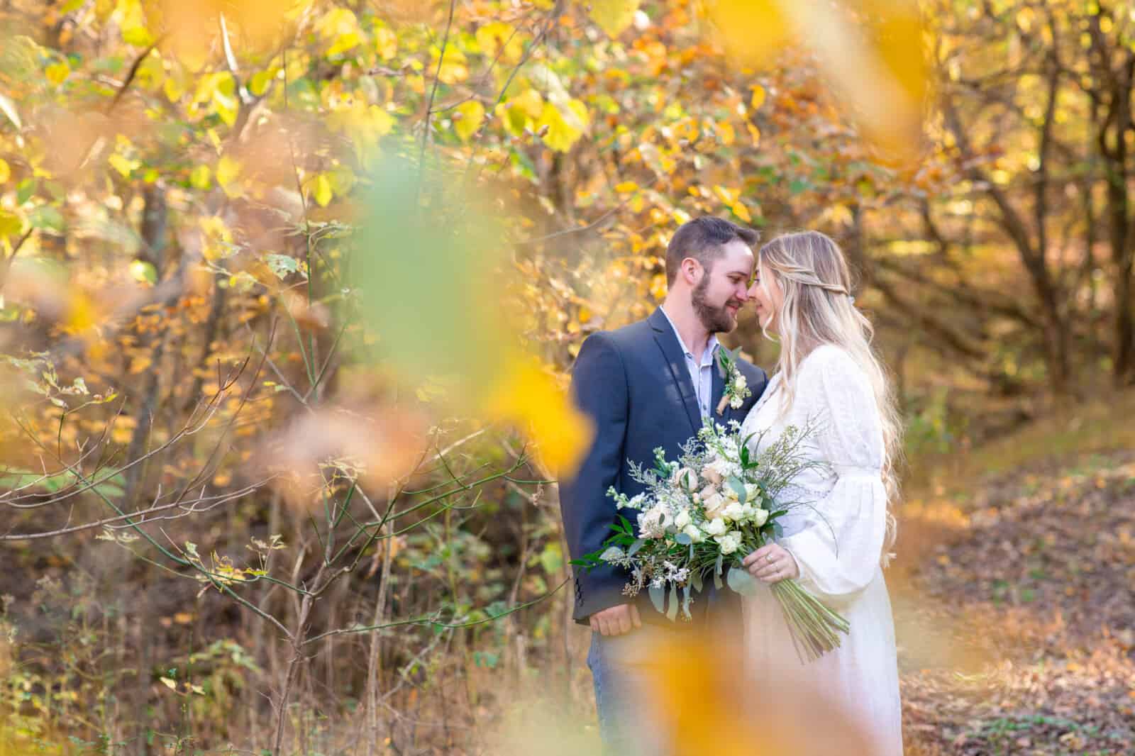 Boho blonde bride with bouquet and groom snuggle in yellow autumn leaves