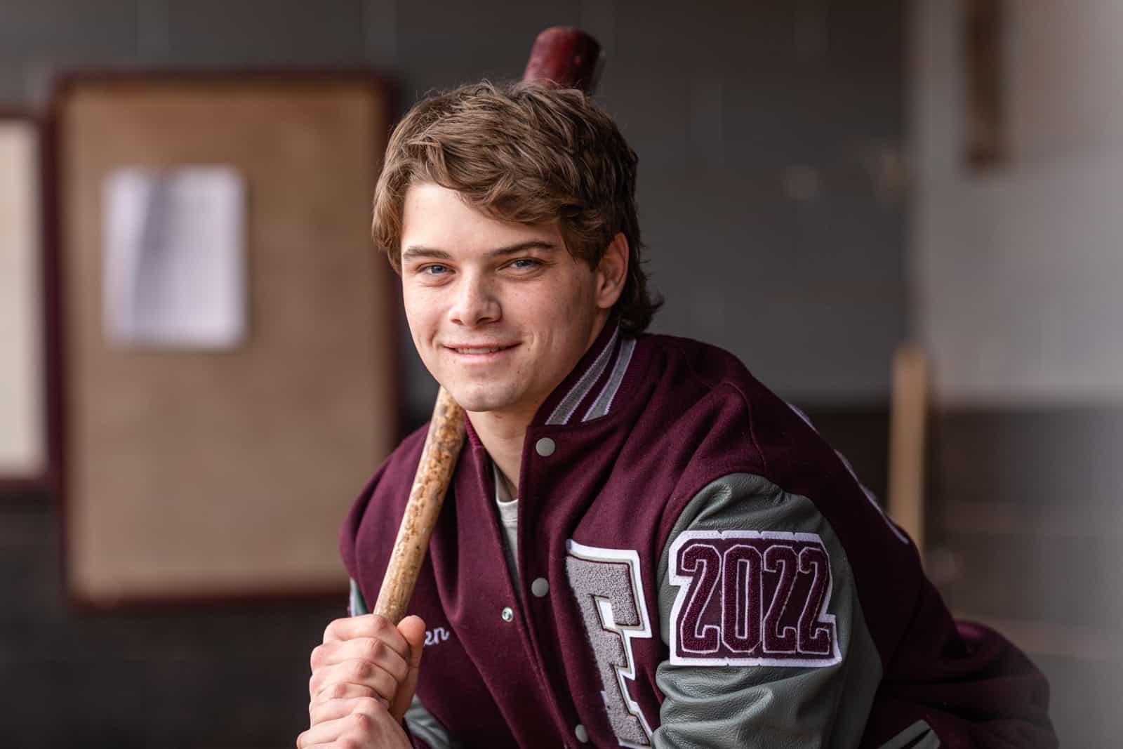 young man in letter jacket holds baseball in dugout