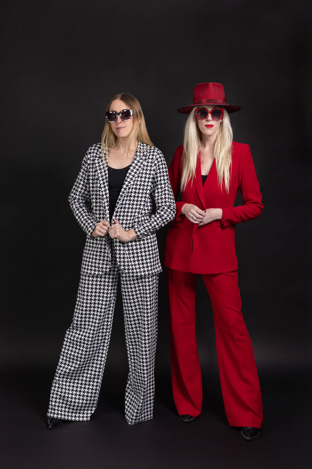 Two blond models pose against black studio background wearing read and black clothes