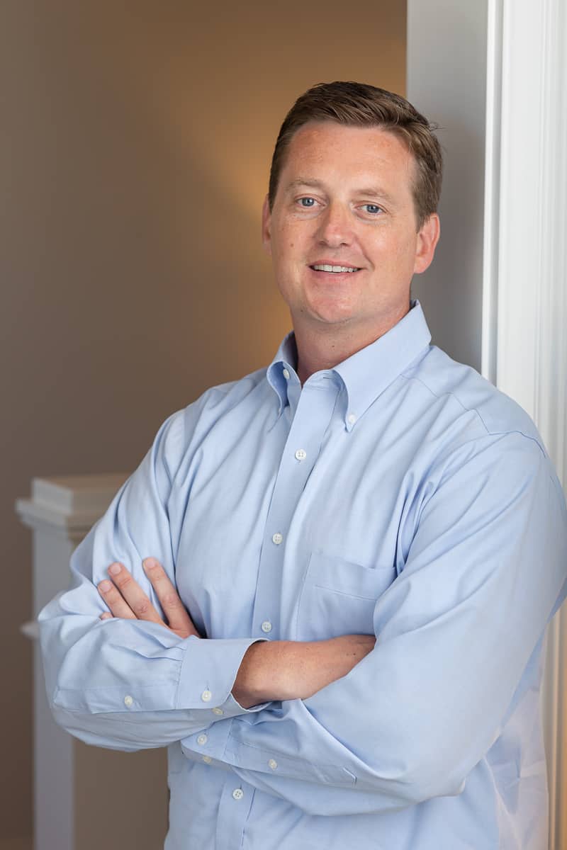 An executive with blue dress shirt leans against a doorframe.