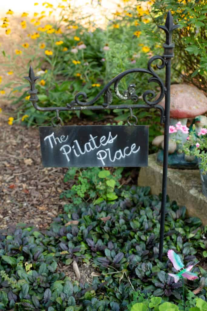 black wrought iron sign in flower garden for The Pilates Place