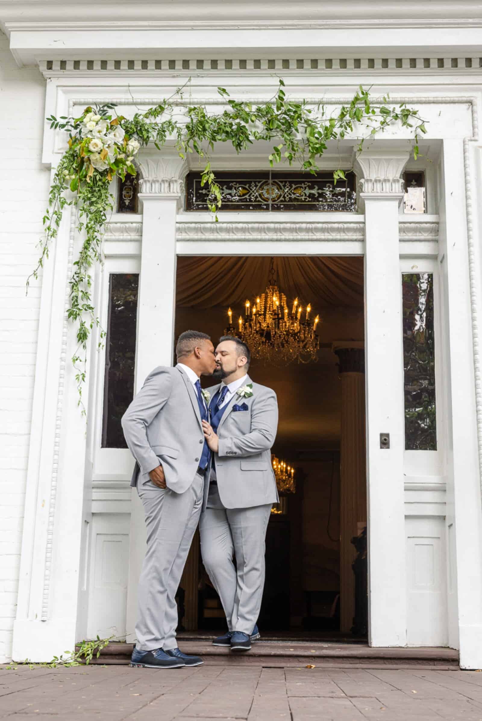 Male same-sex couple portraits outside white southern mansion under floral trellis