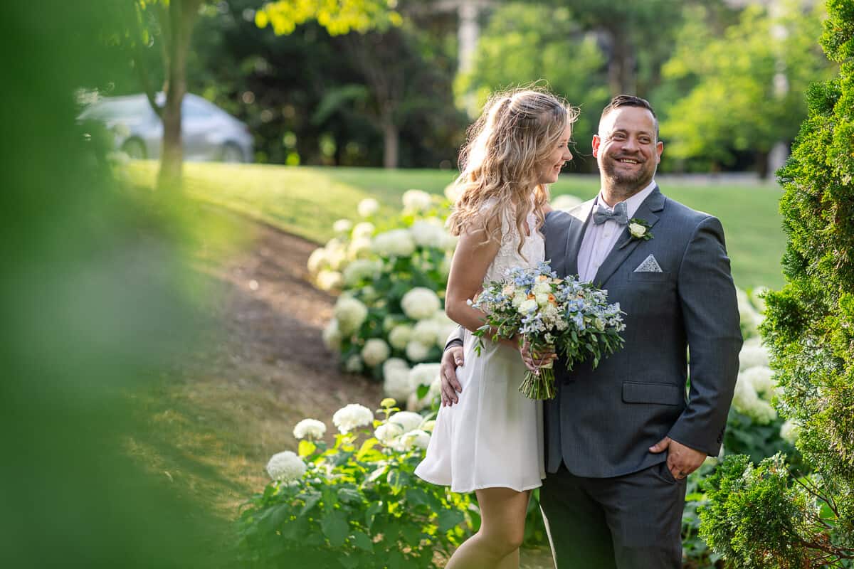 bride and groom laughing in park garden with hydrangeas after elopement