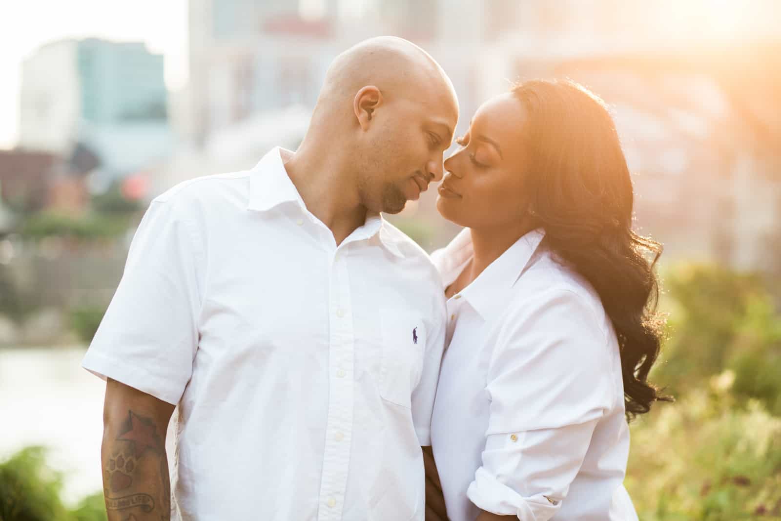 African American couple gaze into each others eyes in an engagement portrait session at sunset with downtown Nashville skyline in background.