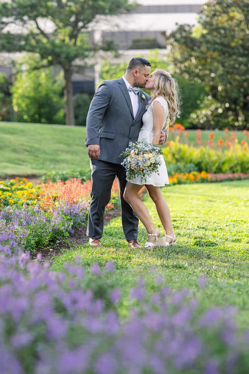 Elopement bride and groom kiss as they take a walk through a flower garden just before sunset