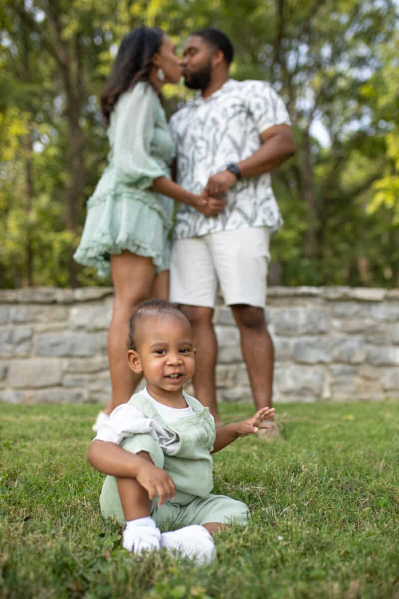 Black couple kisses while their one-year old sits and laughs.