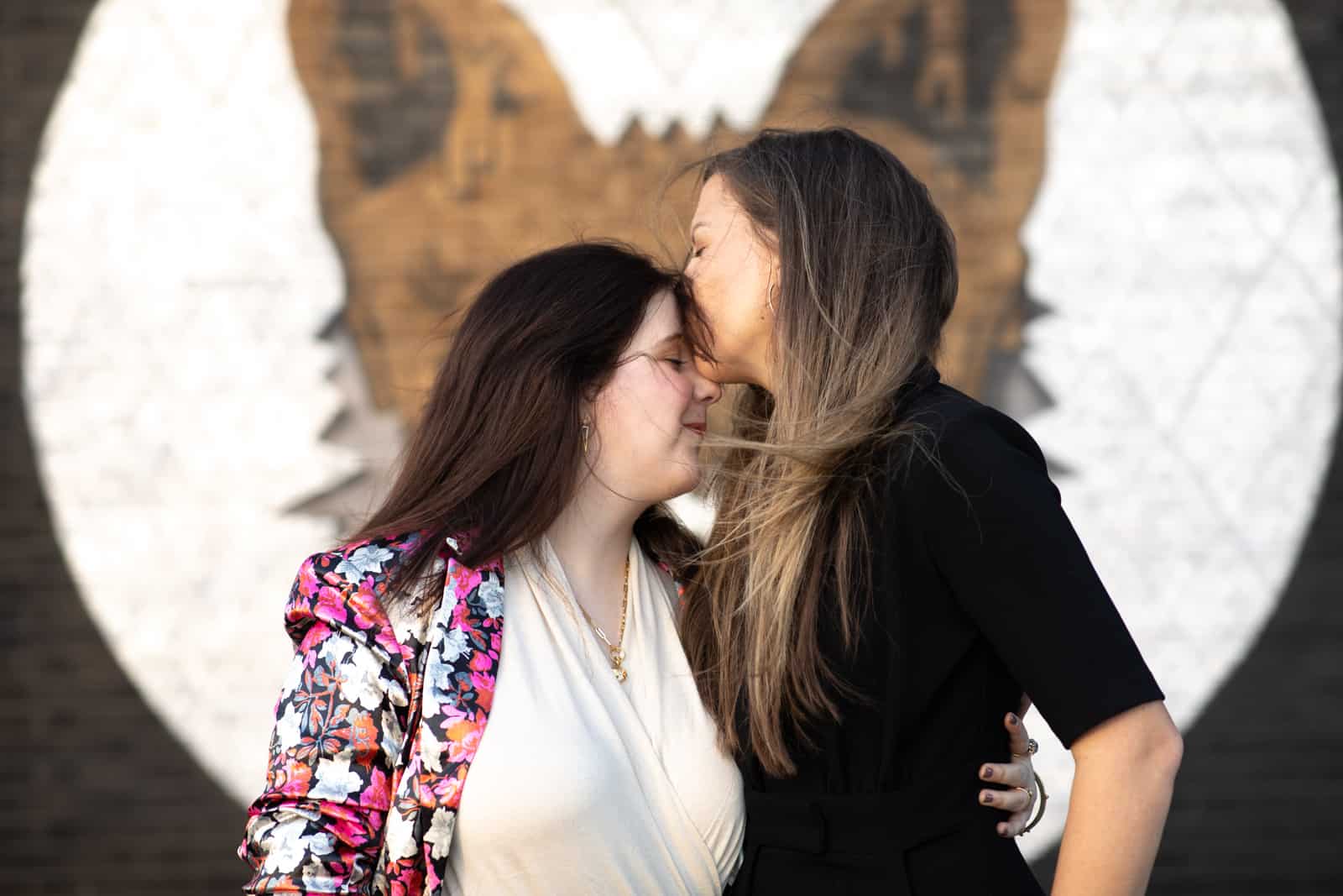 Female same-sex couple kissing in from of mural