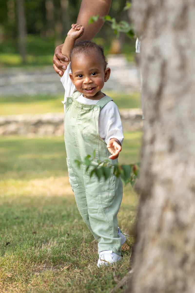 One year old black boy smiling and playing under the trees at the park.