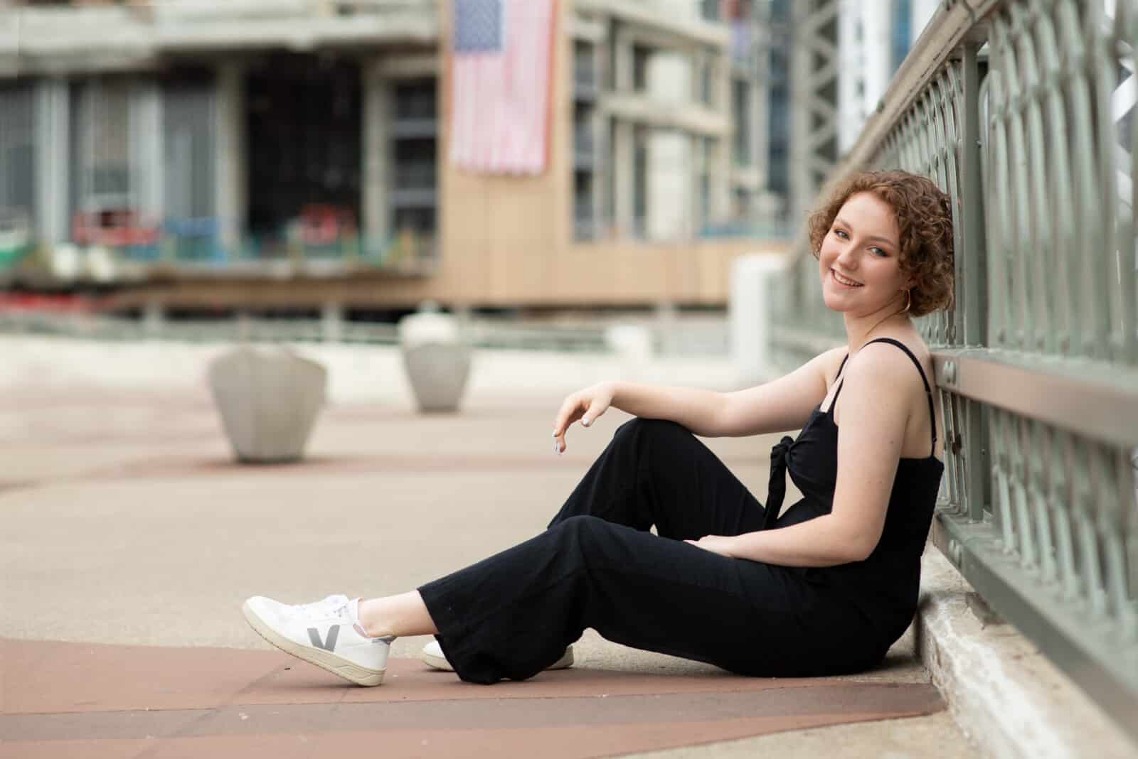 senior portrait of girl leaning back on bridge wearing black jumpsuit