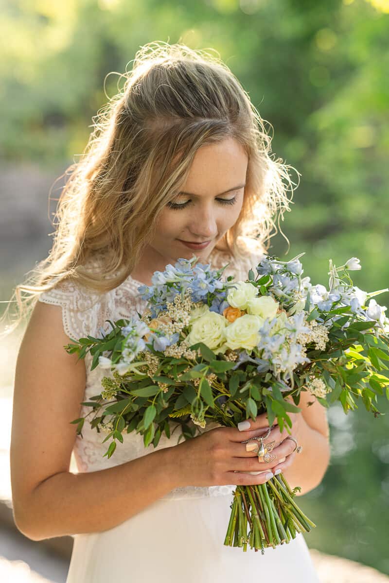 young bride smells flowers from her bouquet with sunset glow