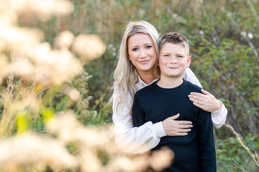 Blond mother embraces her 10 year old son from behind; they both look at camera