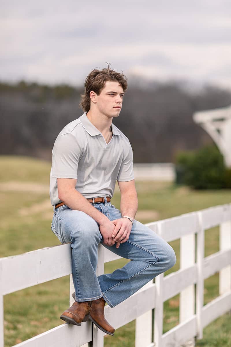 young man in jeans sitting on fence