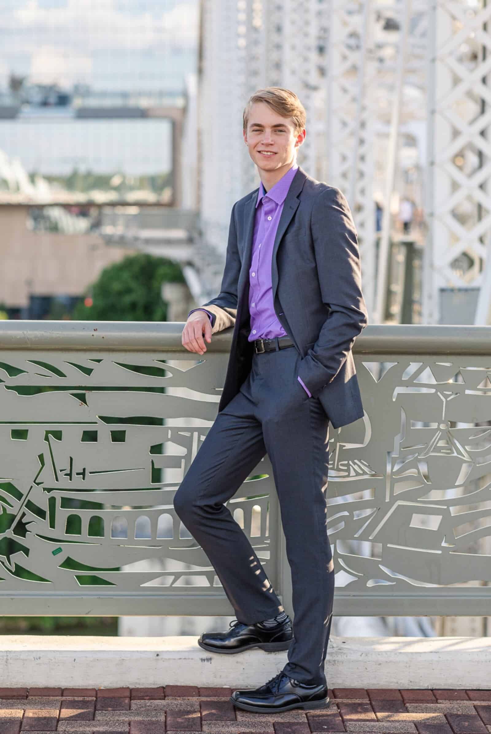 Senior boy in gray suit and purple shirt poses on bridge in Nashville