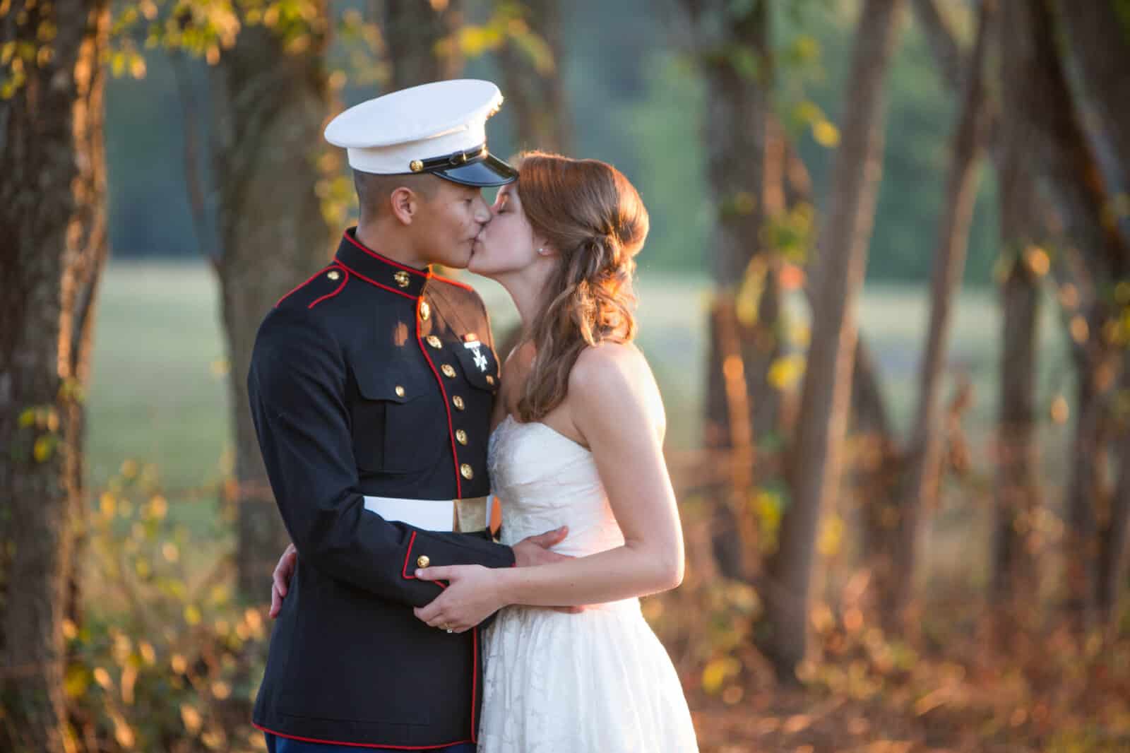 Marine groom in dress blues kissing his bride at sunset in a country field.