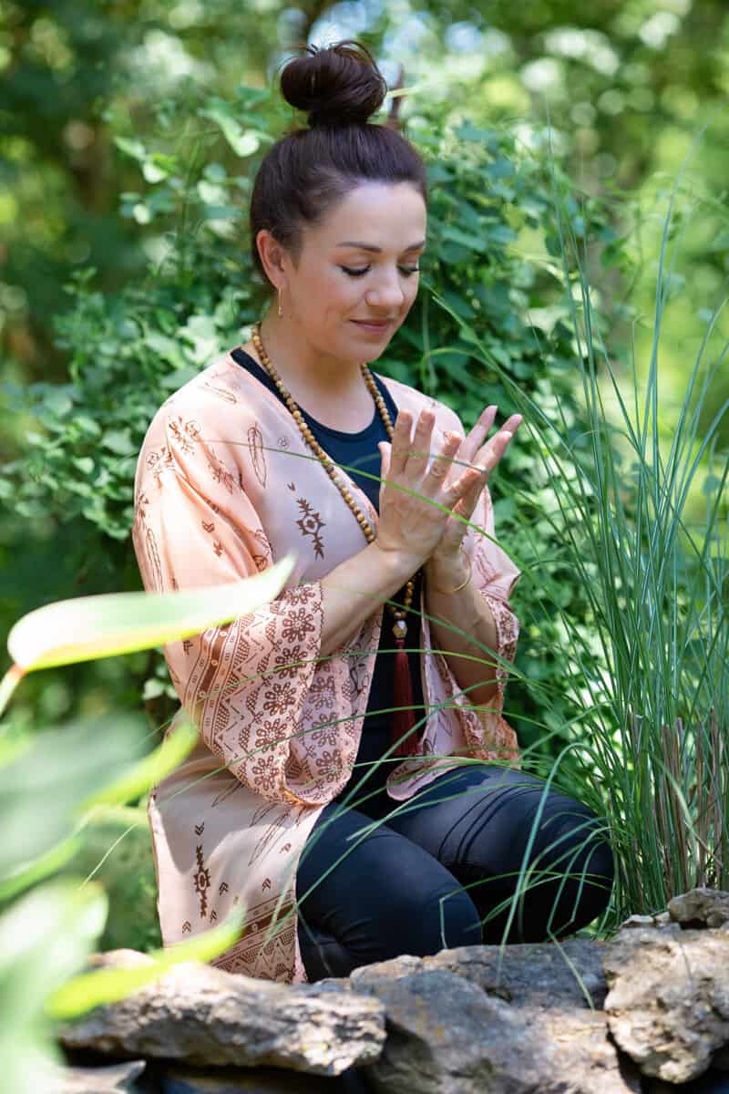 woman in garden kneeling and meditating with hand mudra