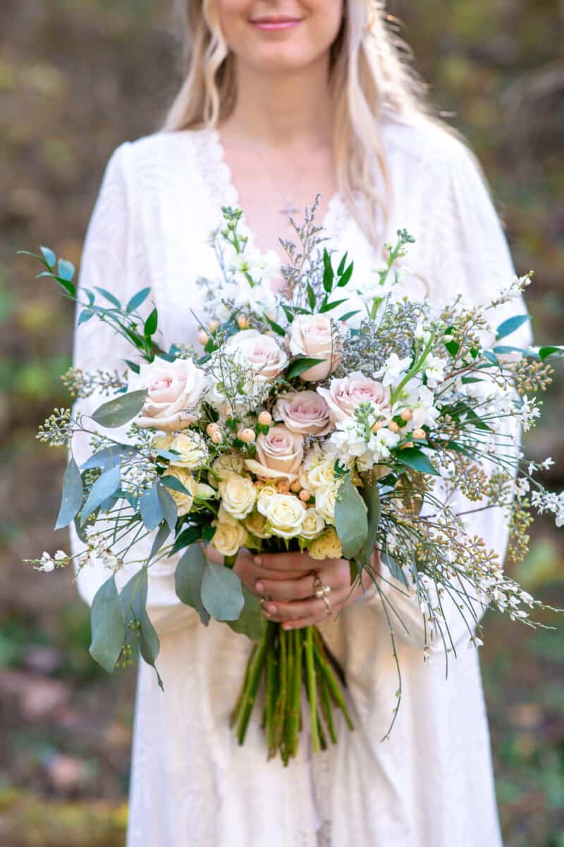 Boho bride with long blond hair holds white and pink bridal bouquet