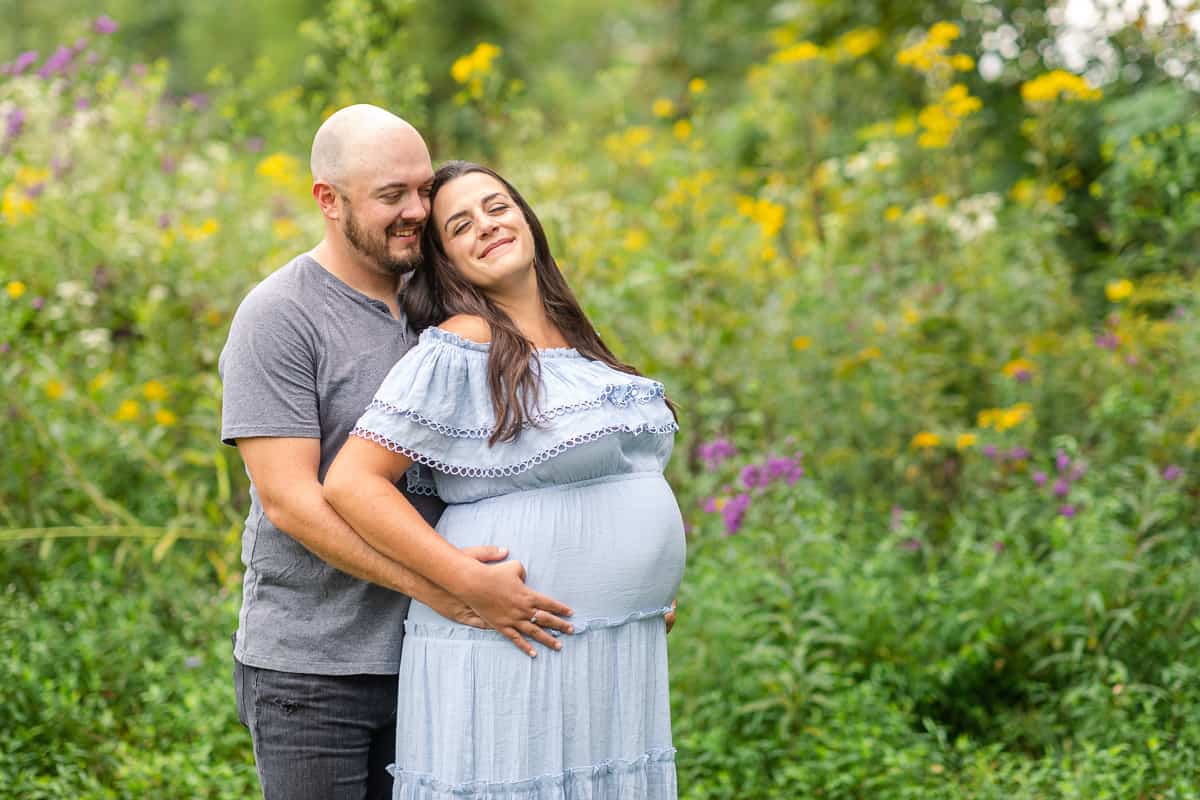 man and pregnant woman in field with wildflowers