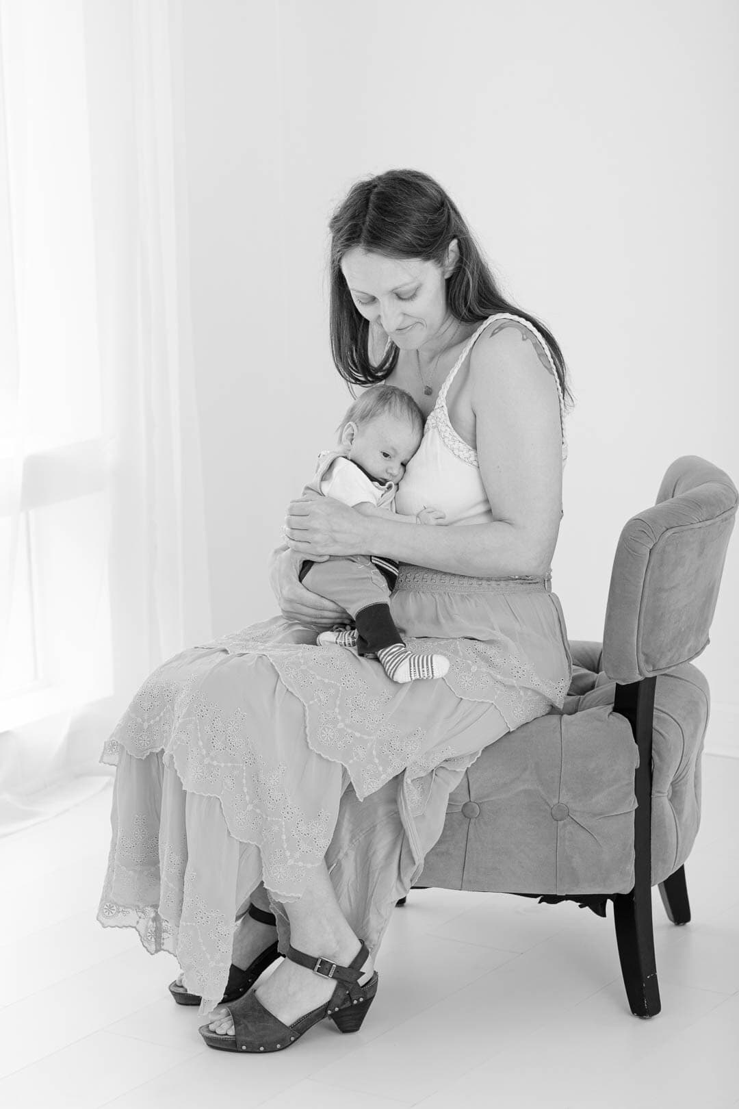 Mother seated in chair cuddles with newborn infant